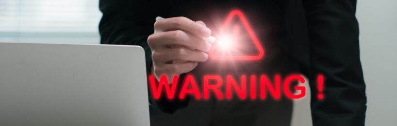 Ein in schwarz gekleideter Mann vor einem Laptop sowie Tablet, der mit einem Digitalstift in die Luft WARNING! schreibt