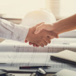 Handschlag über Bauplänen zum erfolgreichen Architektenvertrag