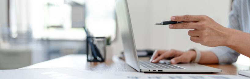 Hand vor Laptop hält Kugelschreiber